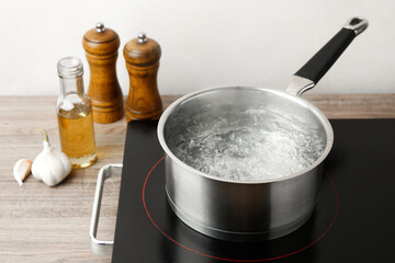 Saucepan with boiling water and stove on wooden table against white background, closeup