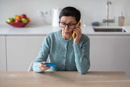 Anxious scared vulnerable woman sending money from accounts to fraudsters on phone. Financial scam, credit card manipulation, identity theft, phone fraud, deception, confusion and exploitation