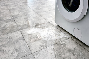 A broken washing machine. Water with detergent flows out from the bottom of the washing machine.