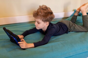 Child engrossed in tablet activity while lying on blue blanket indoors during daytime