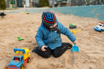 Young child plays in a sandbox with colorful toy trucks on a sunny day at a playground