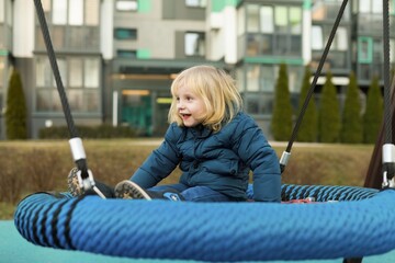 Child enjoys swinging on a large tire swing in a modern park setting during the afternoon