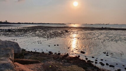 Fototapeta premium Tranquil Sunset Over Calm Ocean with Rocky Shoreline and Reflection on Water Surface