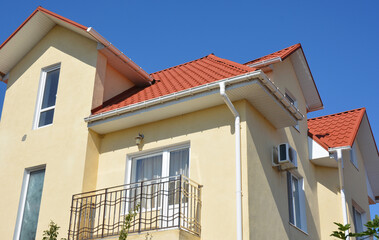 Yellow house facade walls with metal balcony, rain gutter pipeline, plastic soffits, fascia and metal roof