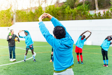 Group of mixed race young people training in a football pitch. Team of young athletes and coach practicing together in a soccer field showing bond and connection