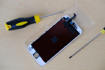Smartphone repair process with screwdriver and disassembled mobile phone on wooden table. Tech...