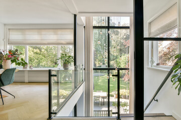 A stylish modern interior showcasing an open staircase and large windows that allow for abundant natural light and a view of the outdoor greenery.