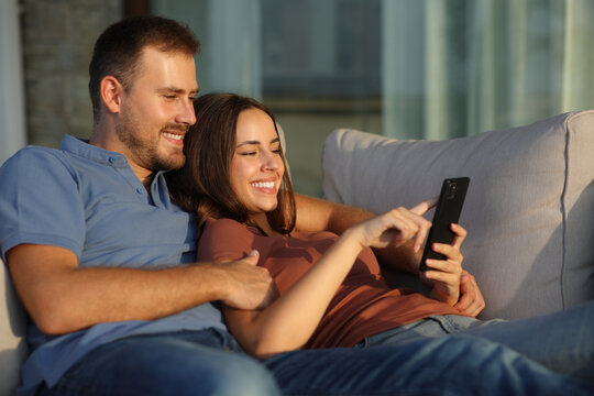 Happy couple using mobile phone in a terrace - Powered by Adobe
