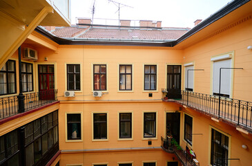 A view of a residential courtyard with yellow walls and multiple windows, featuring balconies with...