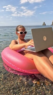 Laptop Beach Work Woman in a pink floatie using a laptop on a beach.