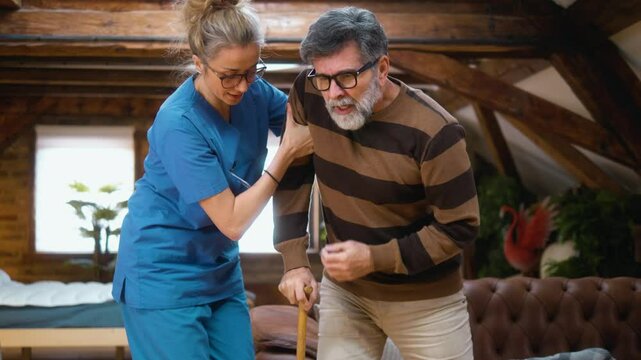 Female caregiver helps a scared elderly 60s man to get up from the floor after a fall accident and mobility problems in the living room at home, he feels instability pains in his back and legs.