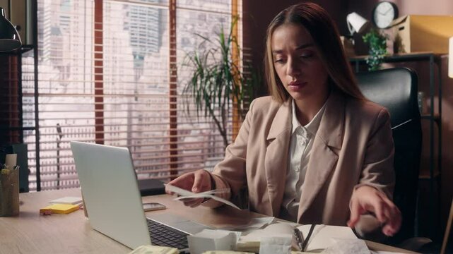 Worried upset shocked Caucasian business woman female girl businesswoman office worker salesman accountant read many bills large check paper money loss crisis shock bankruptcy tax work laptop indoors