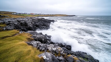 Fototapeta premium Coastal waves crash against rocks. A village sits on the horizon