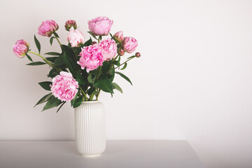 Beautiful bouquet of pink peony flowers in full bloom in vase against white background. Copy space for text.
