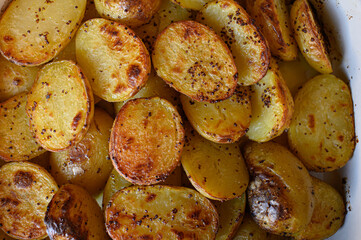 Baked potato halves with a crispy golden crust, seasoned with spices and drizzled with oil. Perfectly roasted potatoes, delicious comfort food, rustic cooking, side dish.