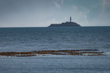 A tall, majestic Rockabill Lighthouse stands proudly on a secluded island, surrounded by calm, serene waters and vibrant kelp beds, enhancing the truly stunning coastal view, Skerries, Ireland