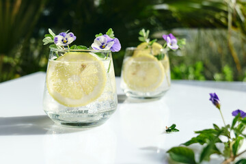 Iced lemonade with edible pansy flowers, lime and mayran. Refreshing summer drink. Healthy organic...