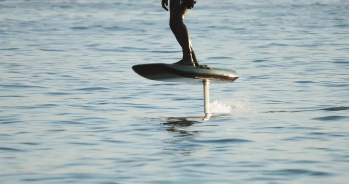 A rider balances on a hydrofoil board gliding across calm sea, with soft lighting and smooth motion captured from distance.. highlighting the joy of balance, motion, and open water