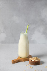 Refreshing oat milk smoothie with straw in glass bottle on gray surface. Detox