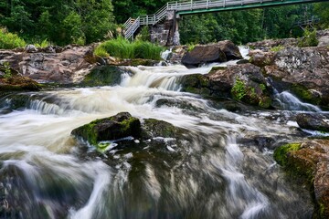 Serene waterfall cascades over moss-covered rocks beneath a wooden bridge in a lush forest