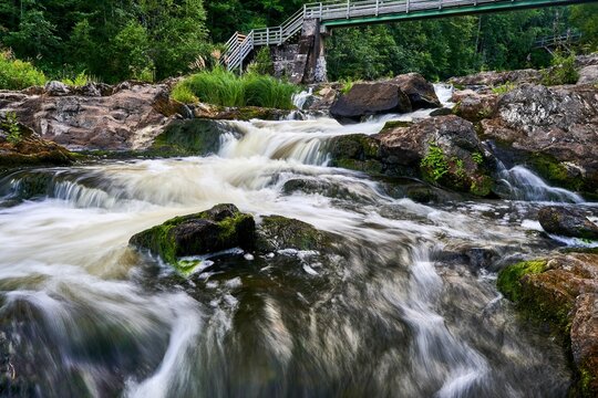 Serene waterfall cascades over moss-covered rocks beneath a wooden bridge in a lush forest