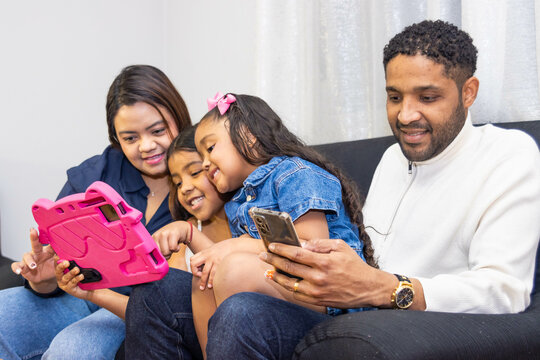 Family enjoying using electronic devices sitting on sofa at home