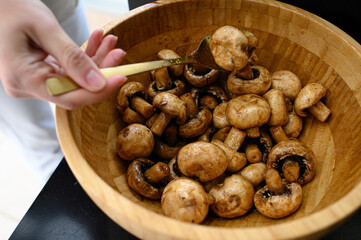 Marinated champignon mushrooms in a wooden bowl, ready for grilling. Fresh, rustic ingredients for outdoor BBQ. Natural light, healthy plant-based cooking scene.