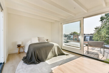 A spacious, modern interior featuring large windows that allow natural light to flood in, creating an inviting and calming atmosphere. A cozy bed adds comfort.