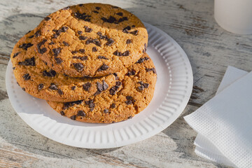 Close-up of a giant chocolate cookie on a disposable plate, accompanied by napkins, cozy morning, and simple joys of life, homemade baking recipe.