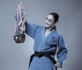 Female martial artist in blue gi holding medals and smiling........4o..
