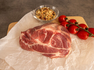 Fresh raw pork meat is placed on crinkled paper alongside ripe cherry tomatoes and cloves of garlic on a rustic wooden board, showcasing an inviting preparation setting.