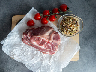 Fresh raw pork meat is placed on crinkled paper alongside ripe cherry tomatoes and cloves of garlic...