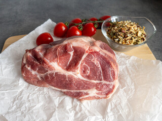 Fresh raw pork meat is placed on crinkled paper alongside ripe cherry tomatoes and cloves of garlic...