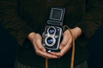 Close up of a caucasian man wearing a green outfit with his hands holding a retro camera with a leather strap on.