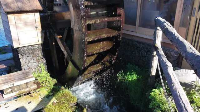 Water flows over a moss covered water wheel, powering a traditional mill in the scenic village of Oshino Hakkai, Japan