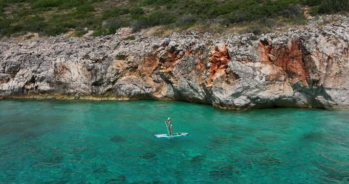 Aerial: Canyon of Gjipe with caucasian woman doing paddle on the Ionian Sea during the day in Vlore County, Albania, establishing drone shot