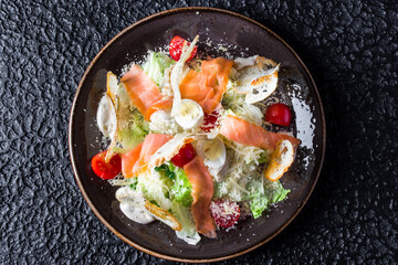 Smoked Salmon Caesar Salad in black plate on black background.