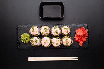 Delicious sushi rolls with wasabi, pickled ginger, and soy sauce on a black slate plate