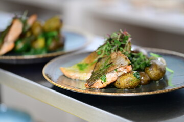 Grilled baked salmon trout served with golden roasted potatoes and wild garlic. Rustic food presentation on a ceramic plate, showcasing a hearty, homemade meal with seasonal ingredients
