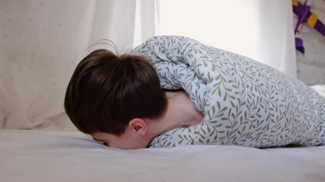 The child was rolled up in a blanket and his feet are tickling. Wrapped boy needs help he is ticklish. Bad joke and game. Psychological problems. Physical touch against will. Unpleasant sensations. 4K