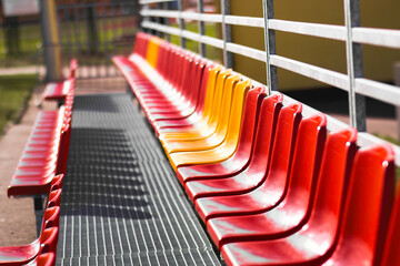 Red and yellow stadium bleachers on a sunny day. Empty spectator seats arranged in rows, creating a vivid geometric pattern. Outdoor sports arena background.

