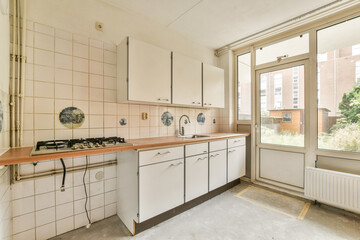 A minimalistic kitchen featuring white cabinets, a gas stove, and large windows allowing plenty of natural light, creating an inviting atmosphere.