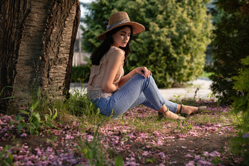 Beautiful young woman sitting under a tree surrounded by spring blossoms, enjoying the serene natural environment and creating a calm, tranquil atmosphere.