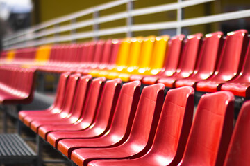 Red and yellow stadium bleachers on a sunny day. Empty spectator seats arranged in rows, creating a vivid geometric pattern. Outdoor sports arena background.

