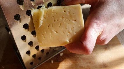 Grate the hard kind of cheese on a grater. Prepare the cheese for cooking. Shredding cheese.