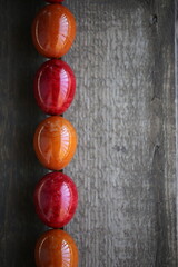 Easter red and orange eggs are lying on the wooden table. The light is beautifully reflected in the eggs through the balcony railing.