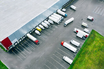 Aerial view of different logistic trucks at the loading docks of a large distribution warehouse. Drone photo.