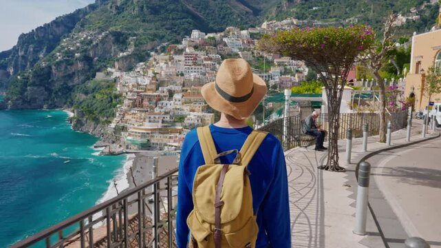 A female tourist in a hat and with a backpack walks through the famous Italian tourist town of Positano on the Amalfi Coast. Positano, Italy