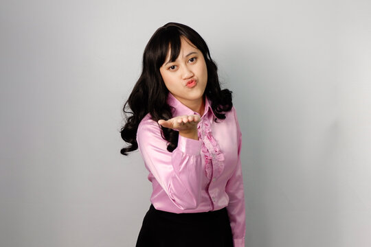 Asian woman with beautiful face wearing pink shirt showcasing kiss gesture from afar.