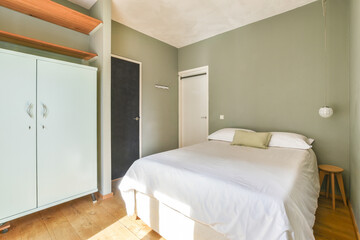 A serene modern bedroom featuring a neatly made bed, light green walls, minimal furniture, and a calming atmosphere ideal for relaxation.